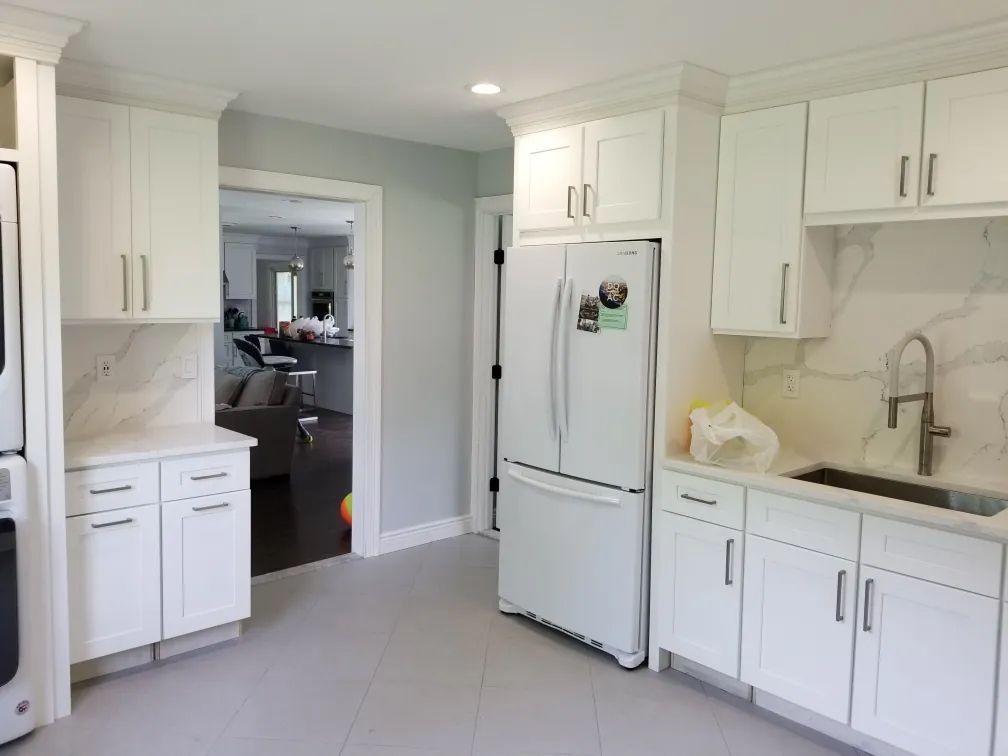 Bright white kitchen with cabinets, sink, stove, and refrigerator, opening to a dining room.