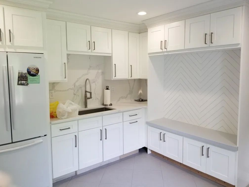 Bright white kitchen with cabinets, refrigerator, sink, and built-in bench seating.
