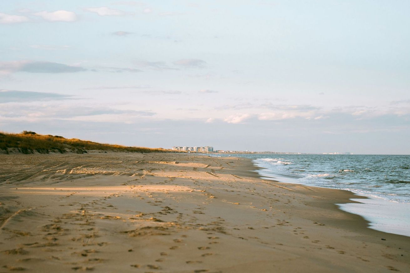 Sandy beach with gentle waves and a distant shoreline under a pale sky