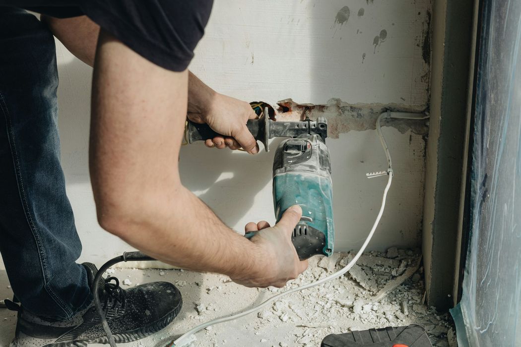 Worker drilling into a wall with a power tool, surrounded by dust and debris in a renovation setting