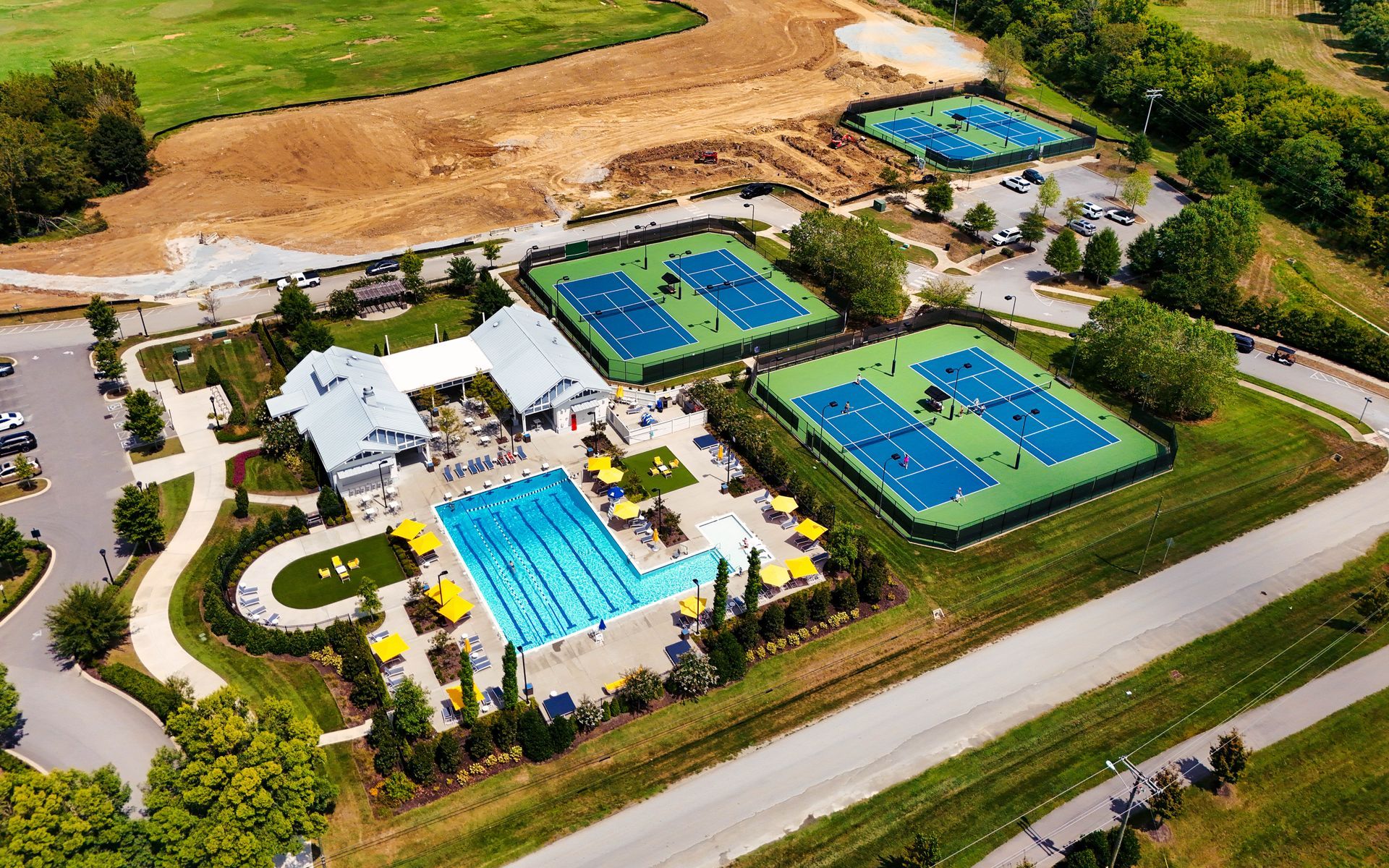 Aerial view of a tennis and swim complex with multiple blue courts, pools, and surrounding greenery.