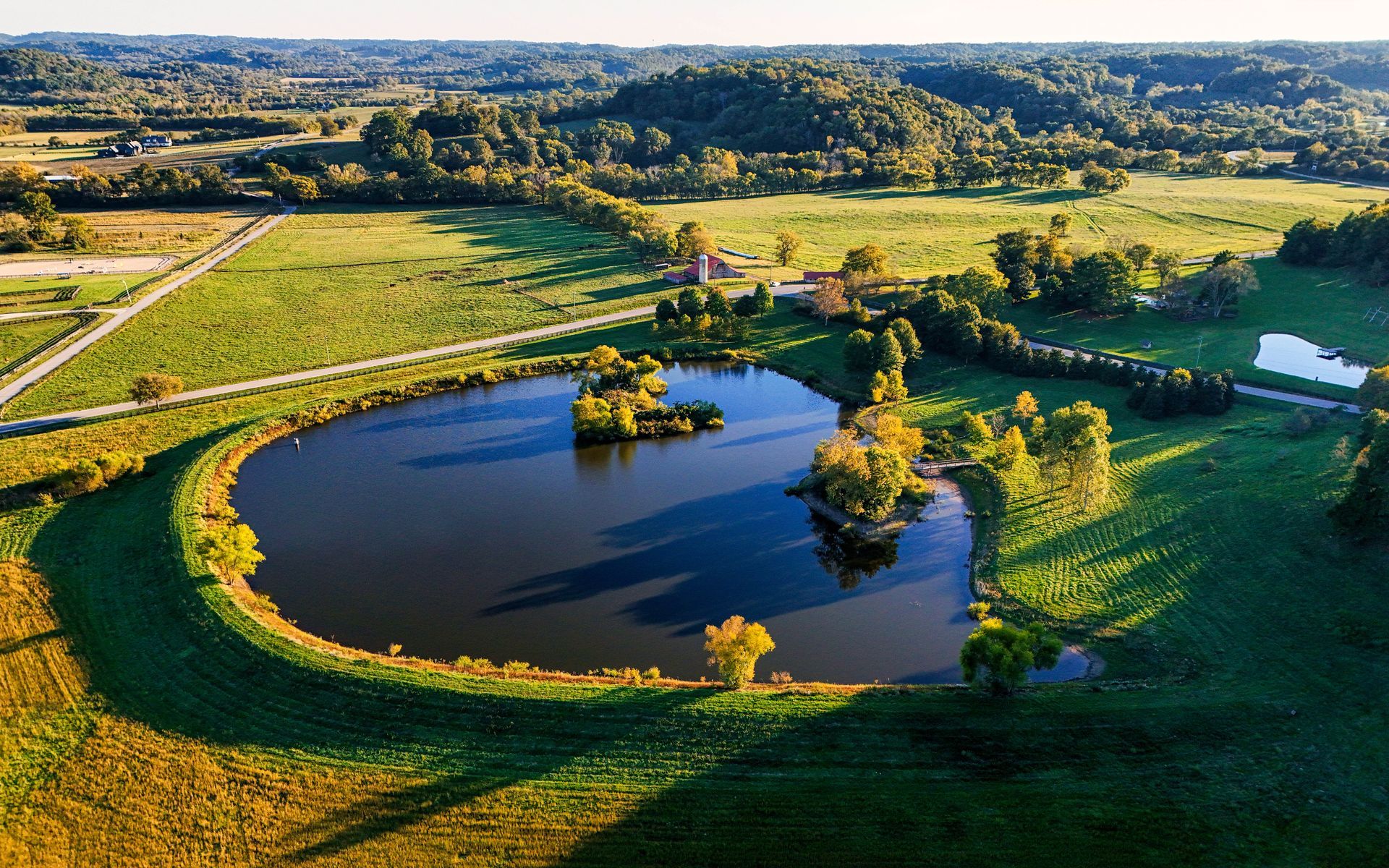 Aerial view of a property with a circular pond surrounded by green fields and trees in the countryside
