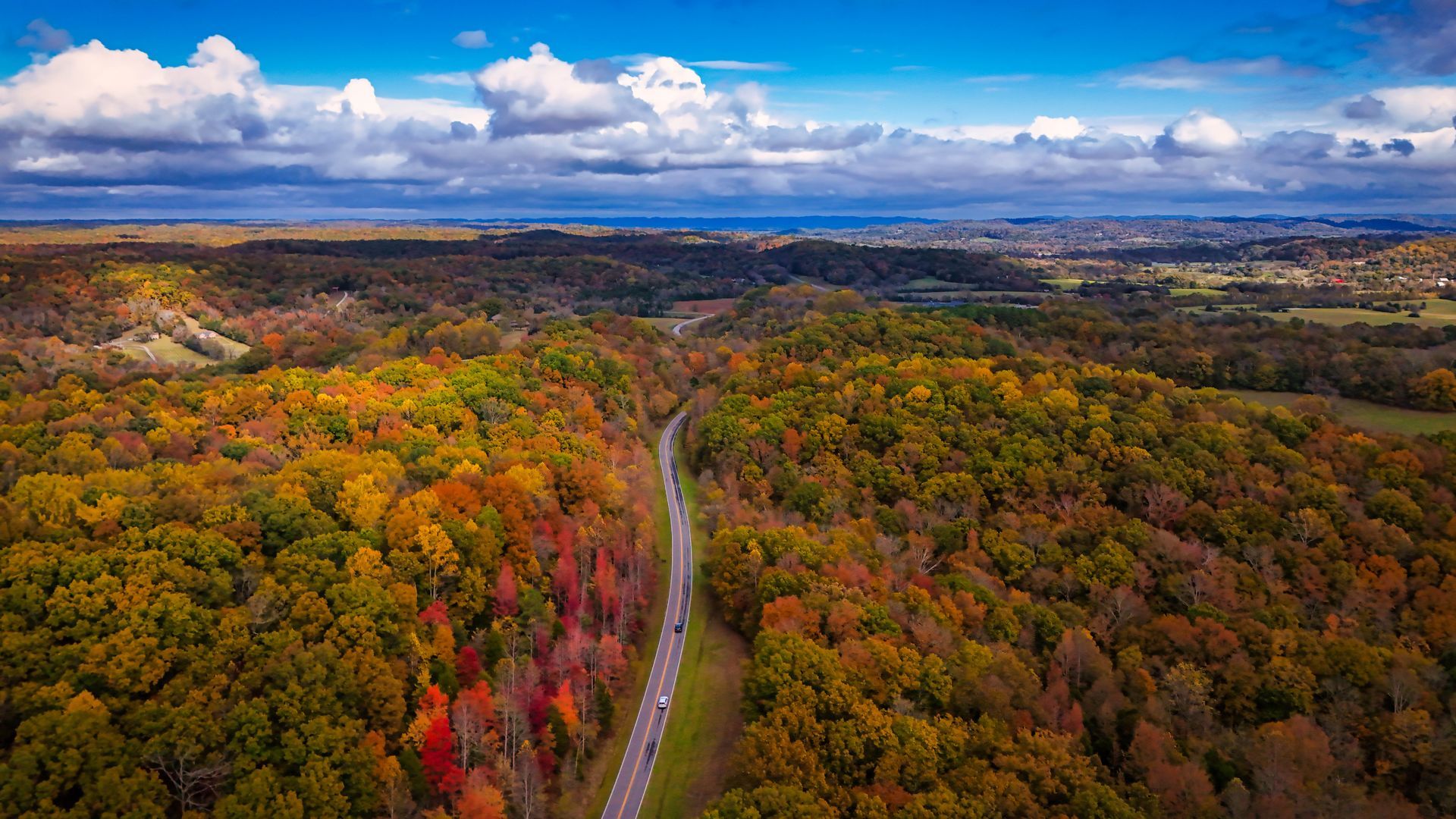 Aerial view of a Natchez Trace through colorful autumn forest under a cloudy blue sky