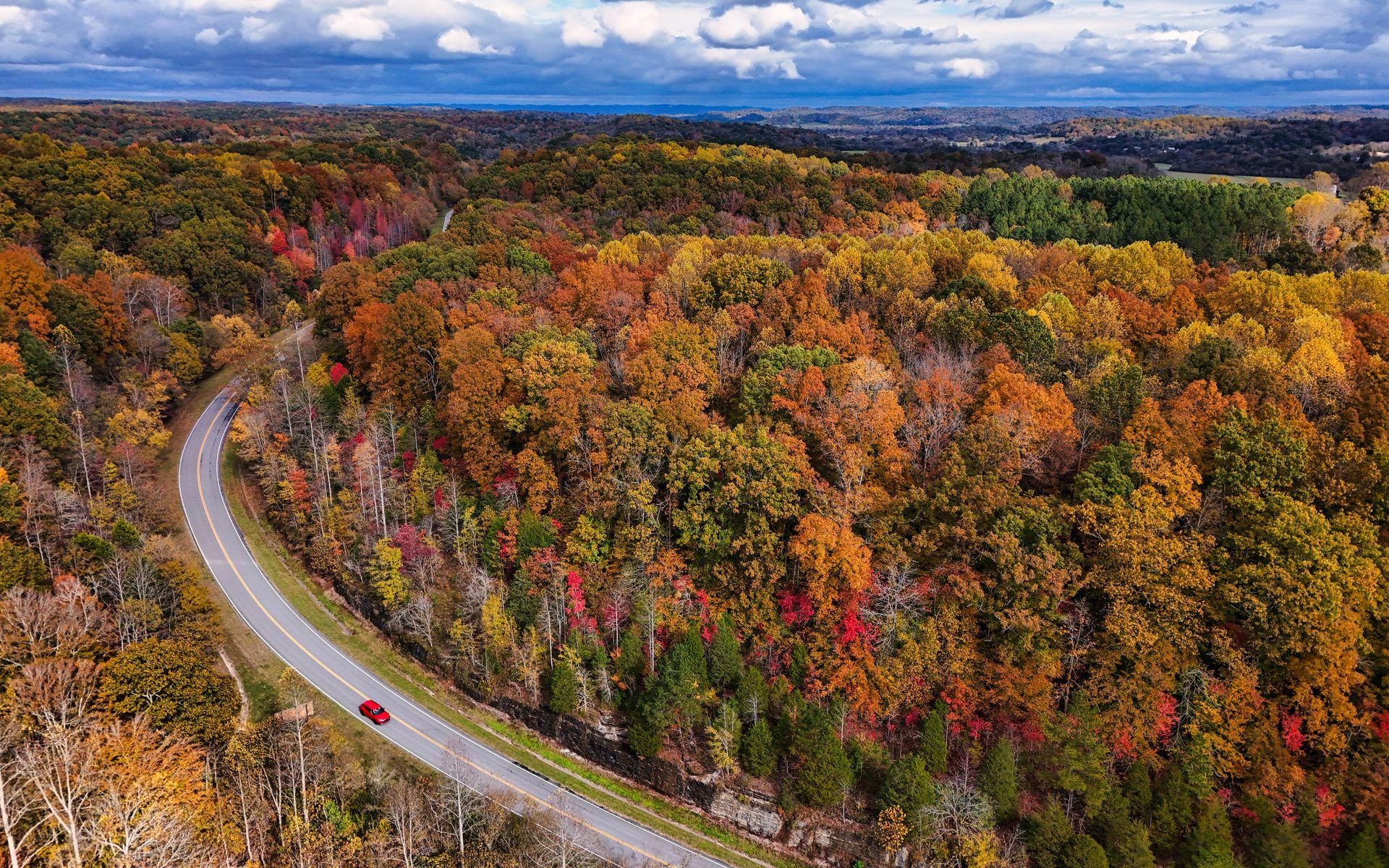 Aerial view of a Natchez Trace through colorful autumn forest under a cloudy blue sky