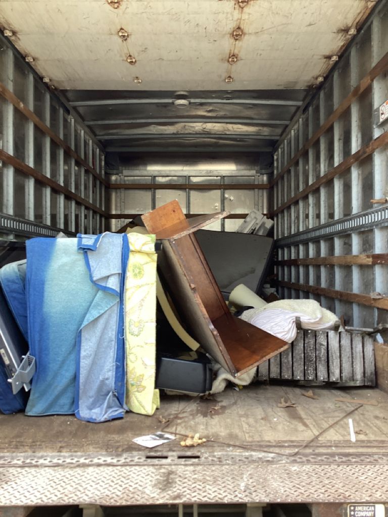 Inside of a box truck partially filled with furniture items covered in moving blankets and protective packing material.