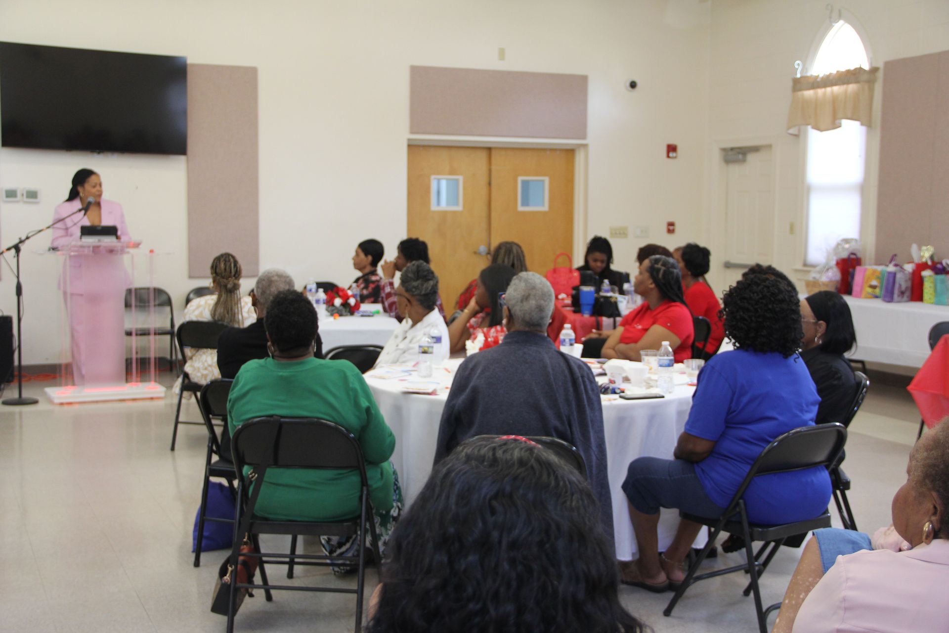 A group of people are sitting at tables in a room with a clock on the wall.