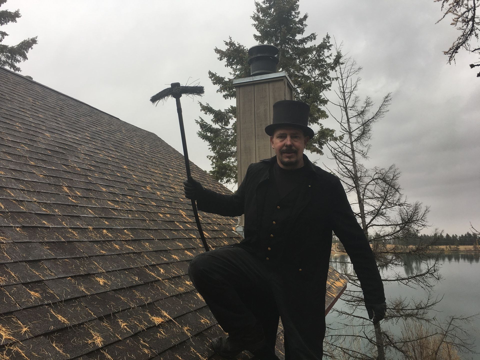 A man in a top hat is holding a chimney brush on a roof.