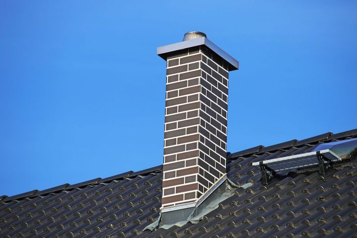 A brick chimney on top of a roof with a blue sky in the background.