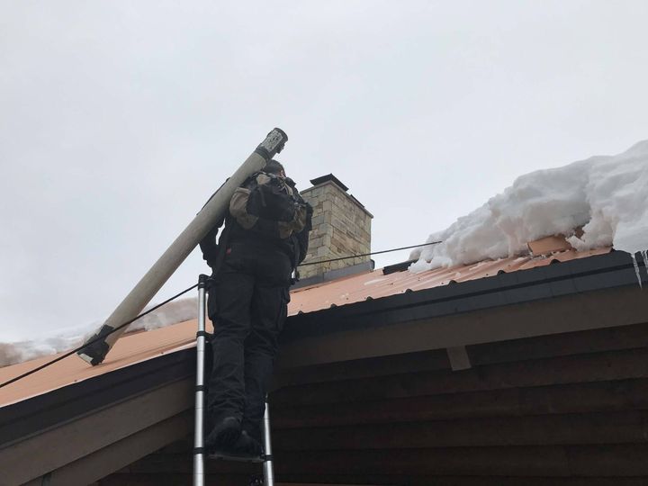 A man standing on a ladder on top of a roof with snow on it