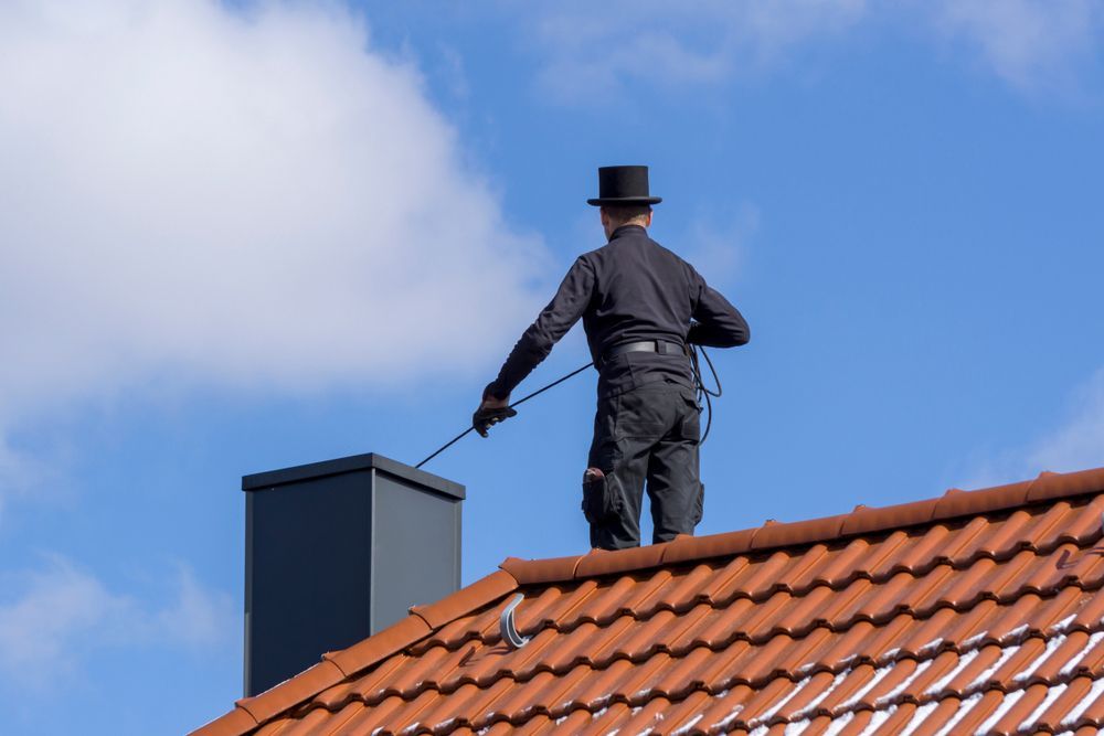 A chimney sweep is standing on top of a tiled roof.