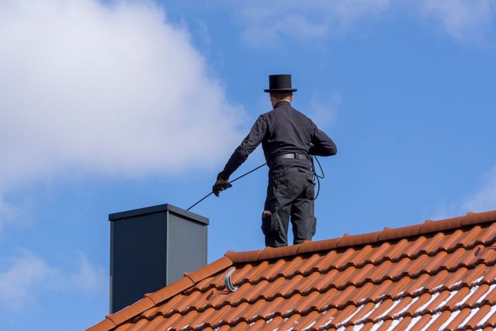 A chimney sweep is standing on top of a tiled roof.