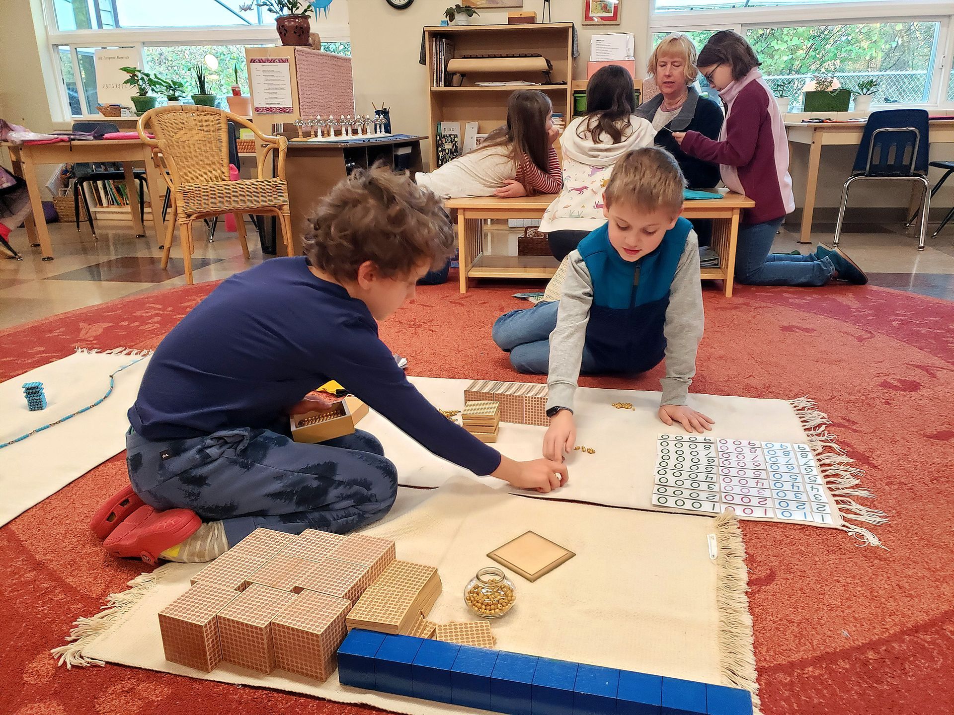 A group of children are working with montessori math blocks on the floor in a classroom.