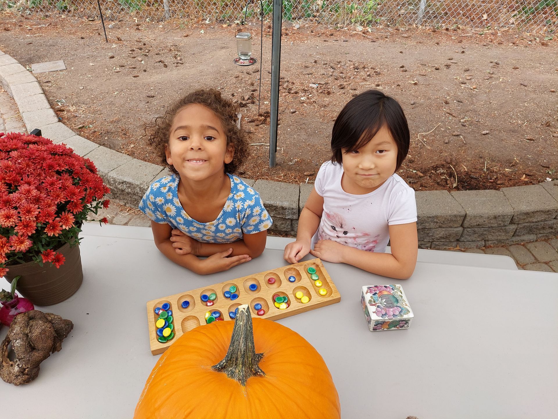 Two little girls are sitting at a table with a pumpkin and a puzzle.