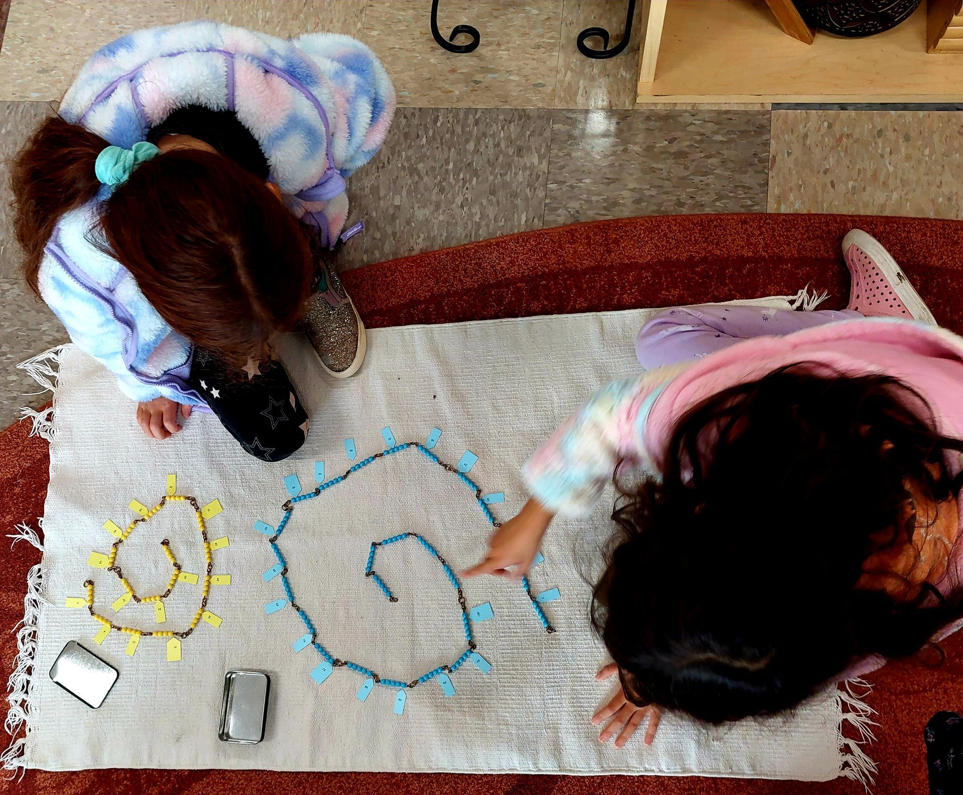 Two girls are laying on a rug working with montessori math materials