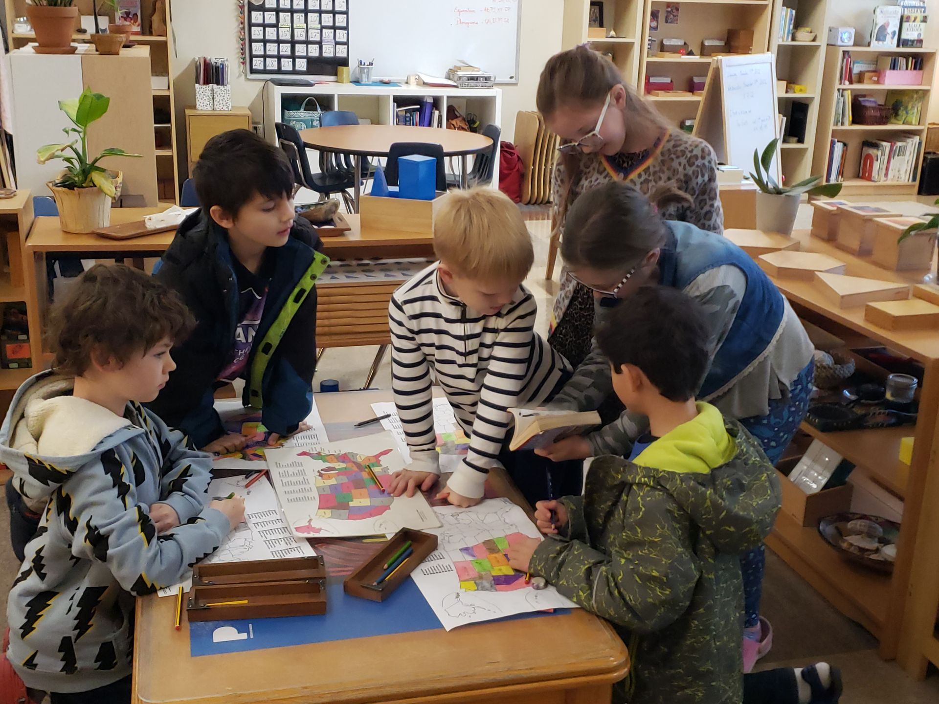A group of children are sitting around a table in a montessori classroom working with color maps
