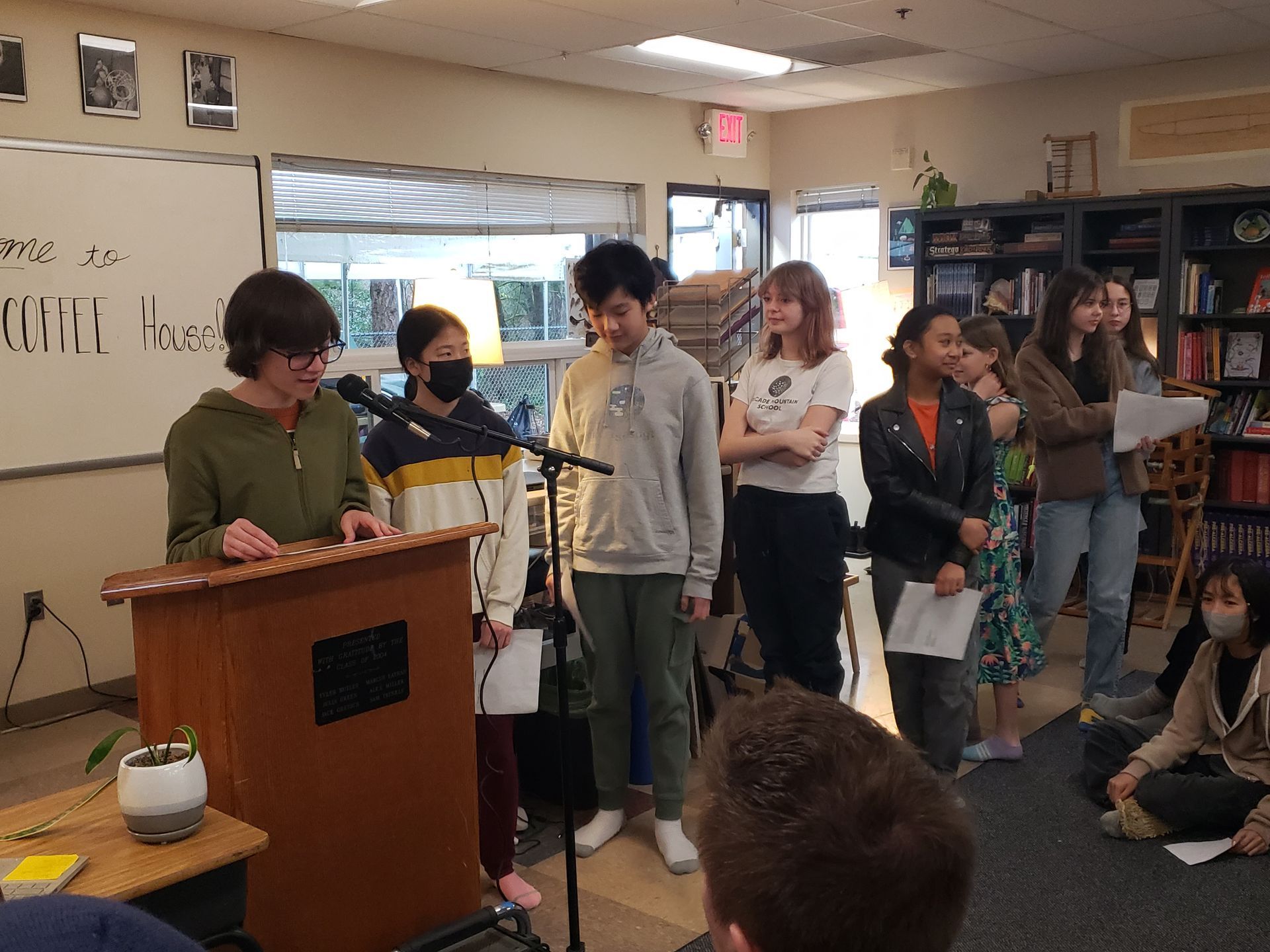 A group of adolescents are standing around a podium in a classroom.