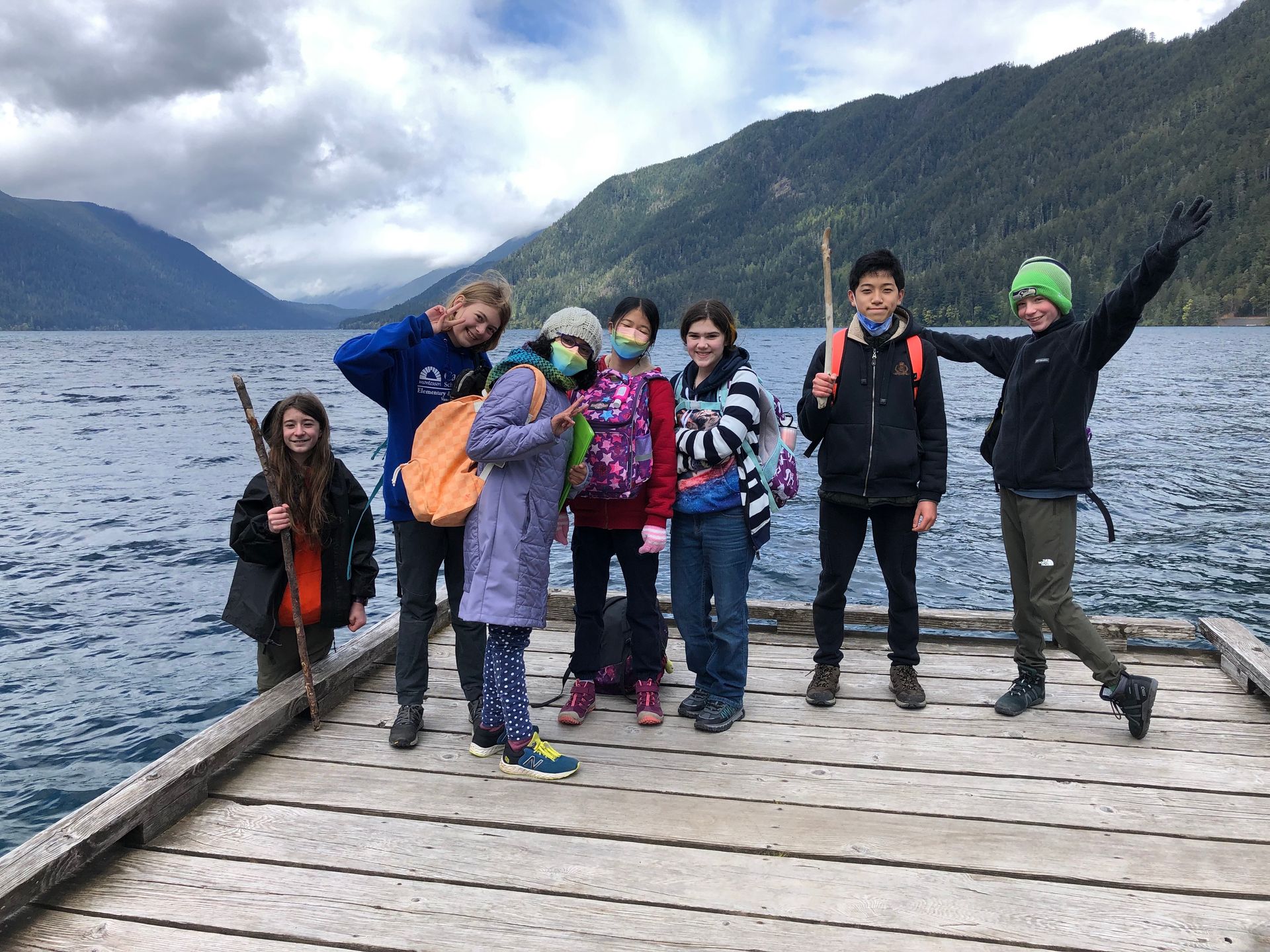 A group of children are standing on a dock next to a lake.