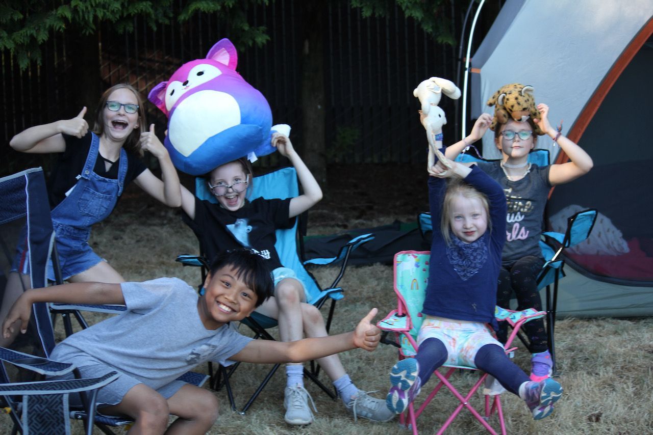 A group of children are posing for a picture in front of a tent with puffed toys in their hands