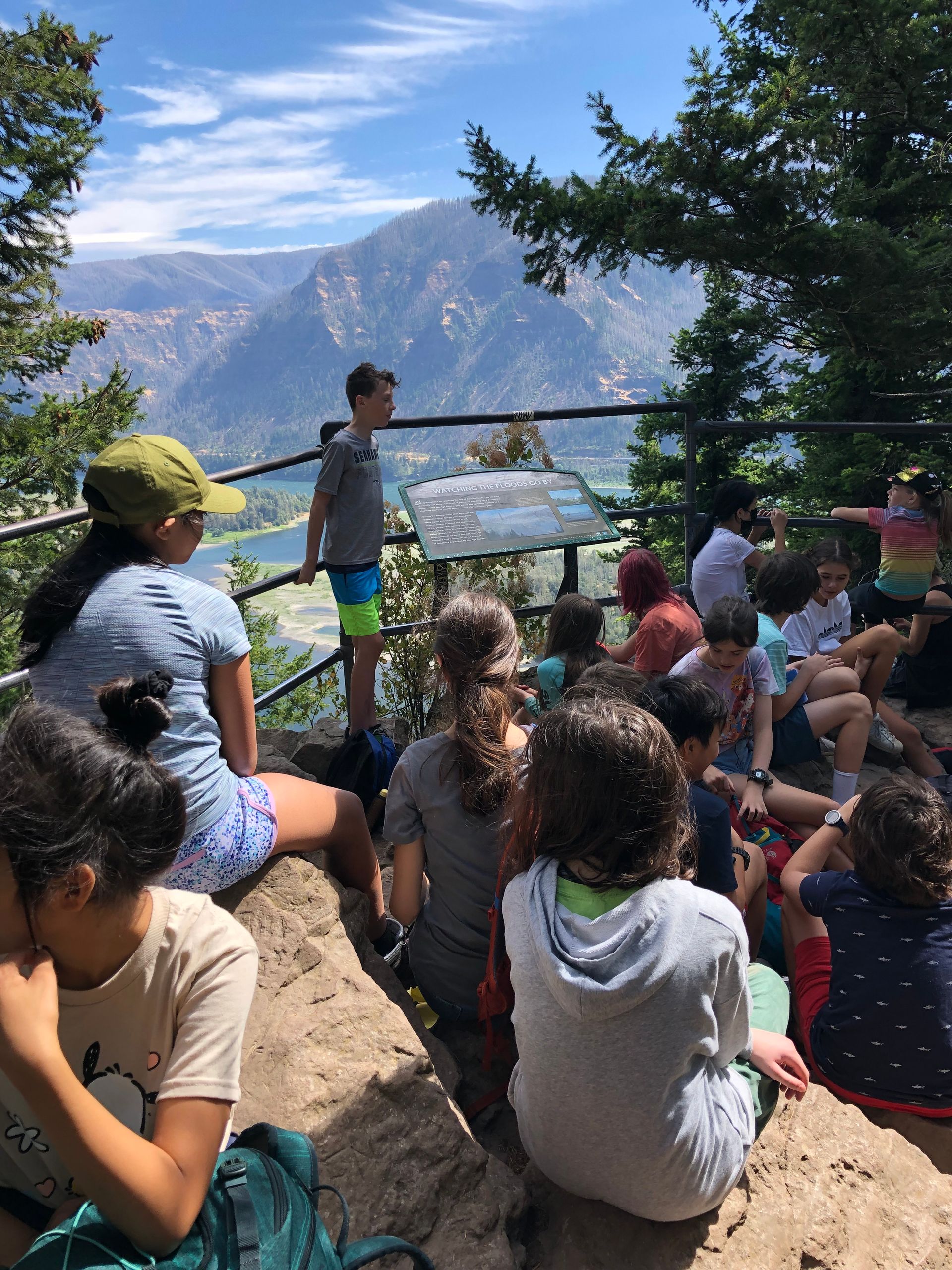 A group of adolescents are sitting on a rock overlooking a mountain.