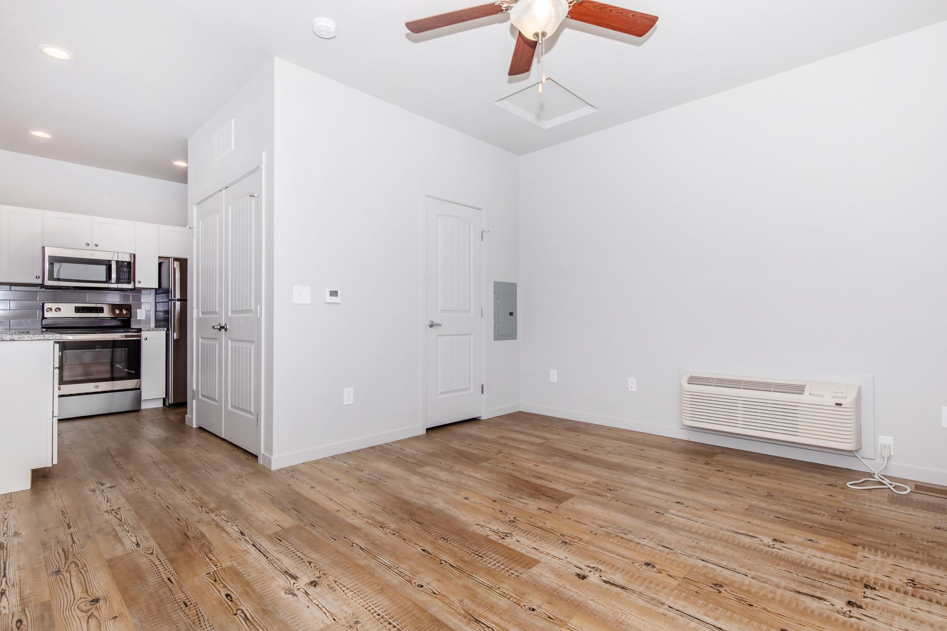Empty bright kitchen-living room with hardwood floors, white walls, and a ceiling fan