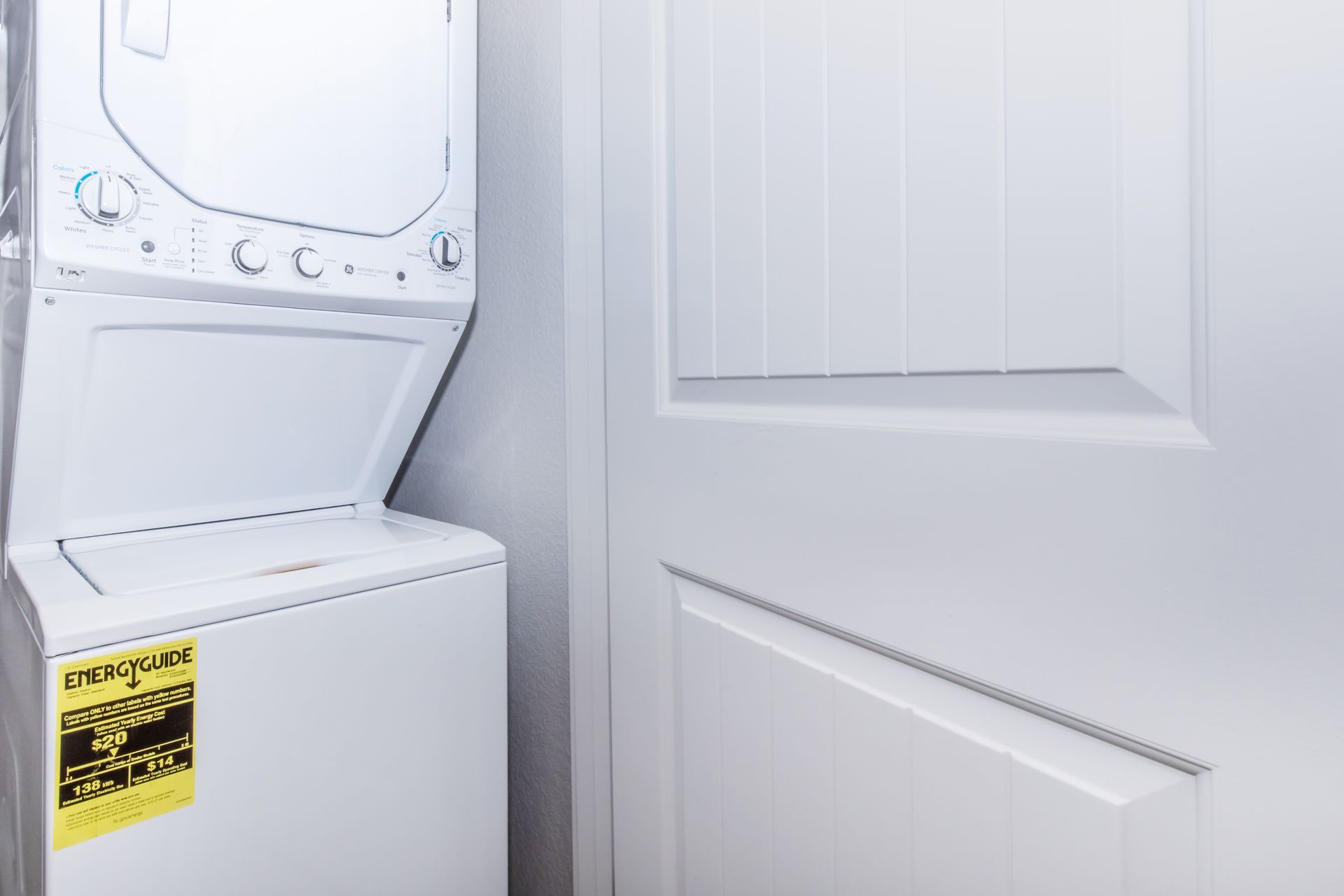 White laundry washer and dryer stacked beside a white door in a small utility area.