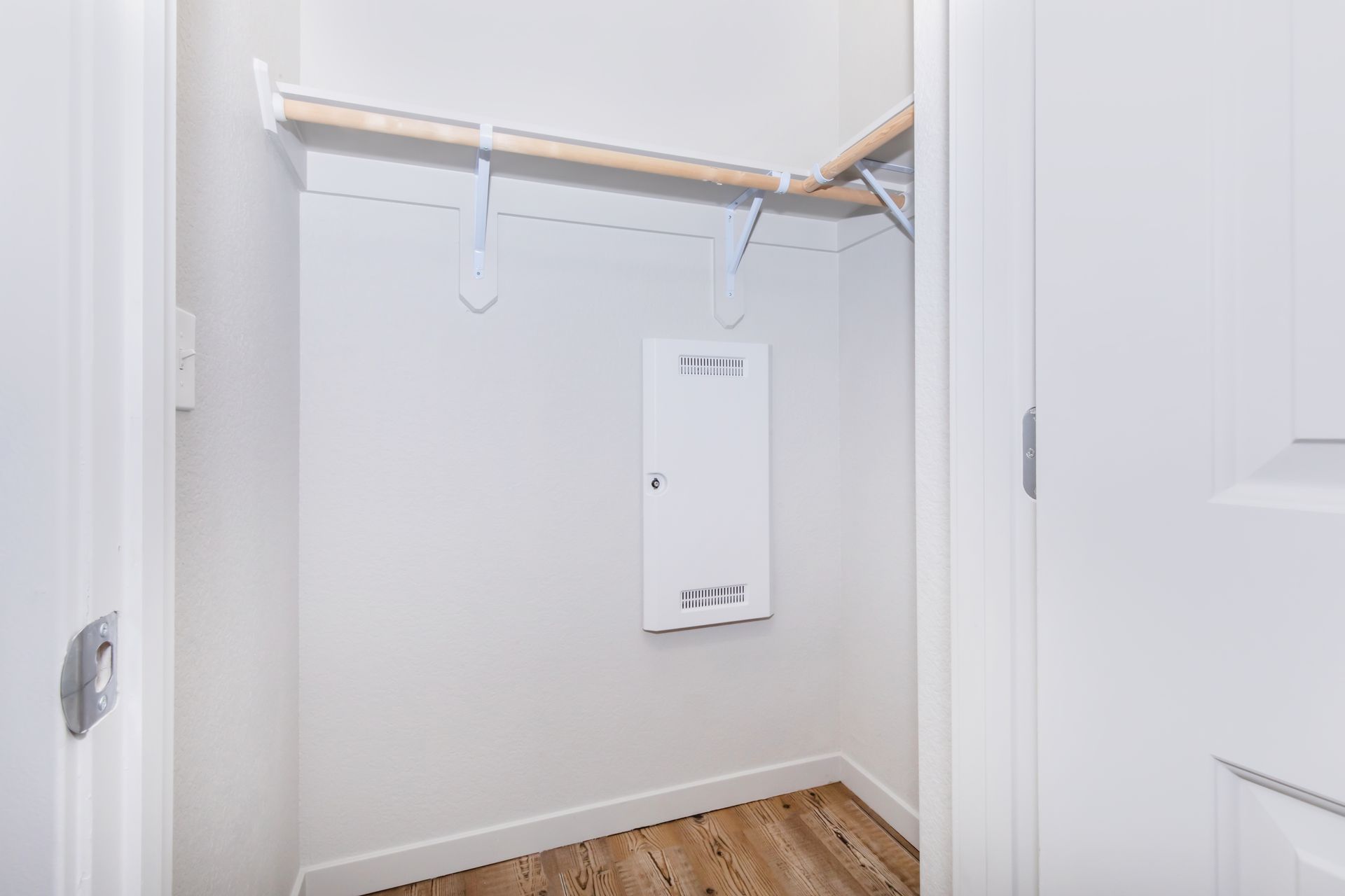 Empty walk-in closet with white walls, wood floor, and hanging rod under a shelf.