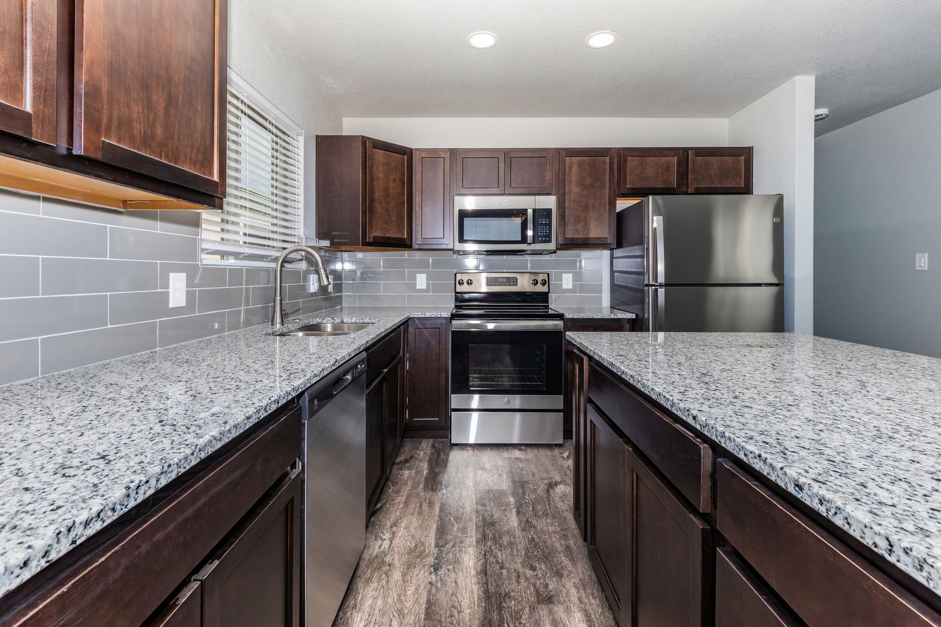 Modern kitchen with dark wood cabinets, speckled countertops, stainless steel appliances, and gray tile backsplash