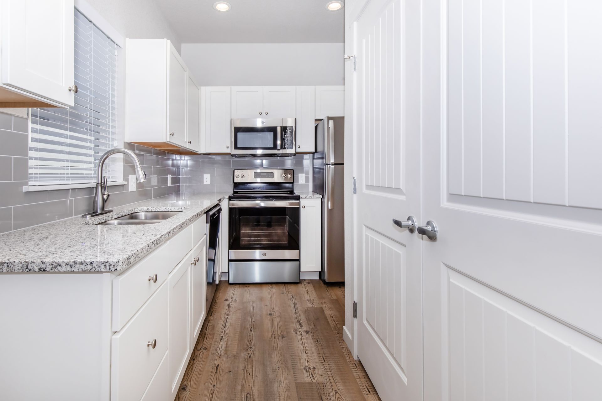 Bright white galley kitchen with stainless steel appliances, granite counters, and wood flooring