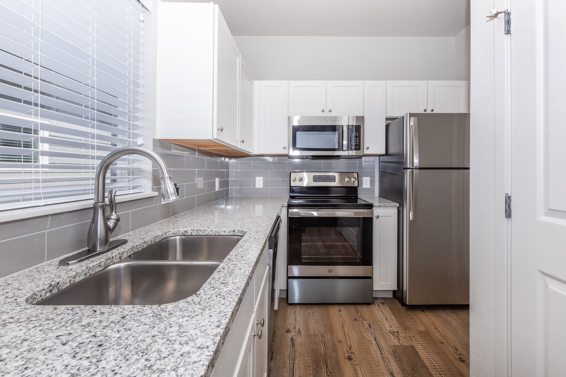 Modern white kitchen with stainless steel appliances, granite counters, and wood floor