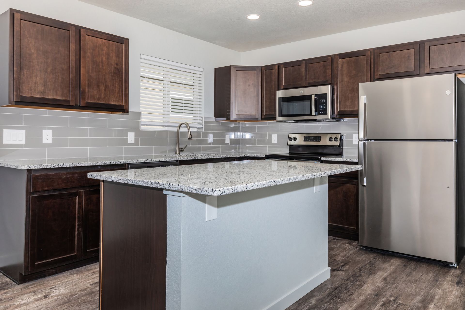 Modern kitchen with dark wood cabinets, stainless steel appliances, and a granite island counter.