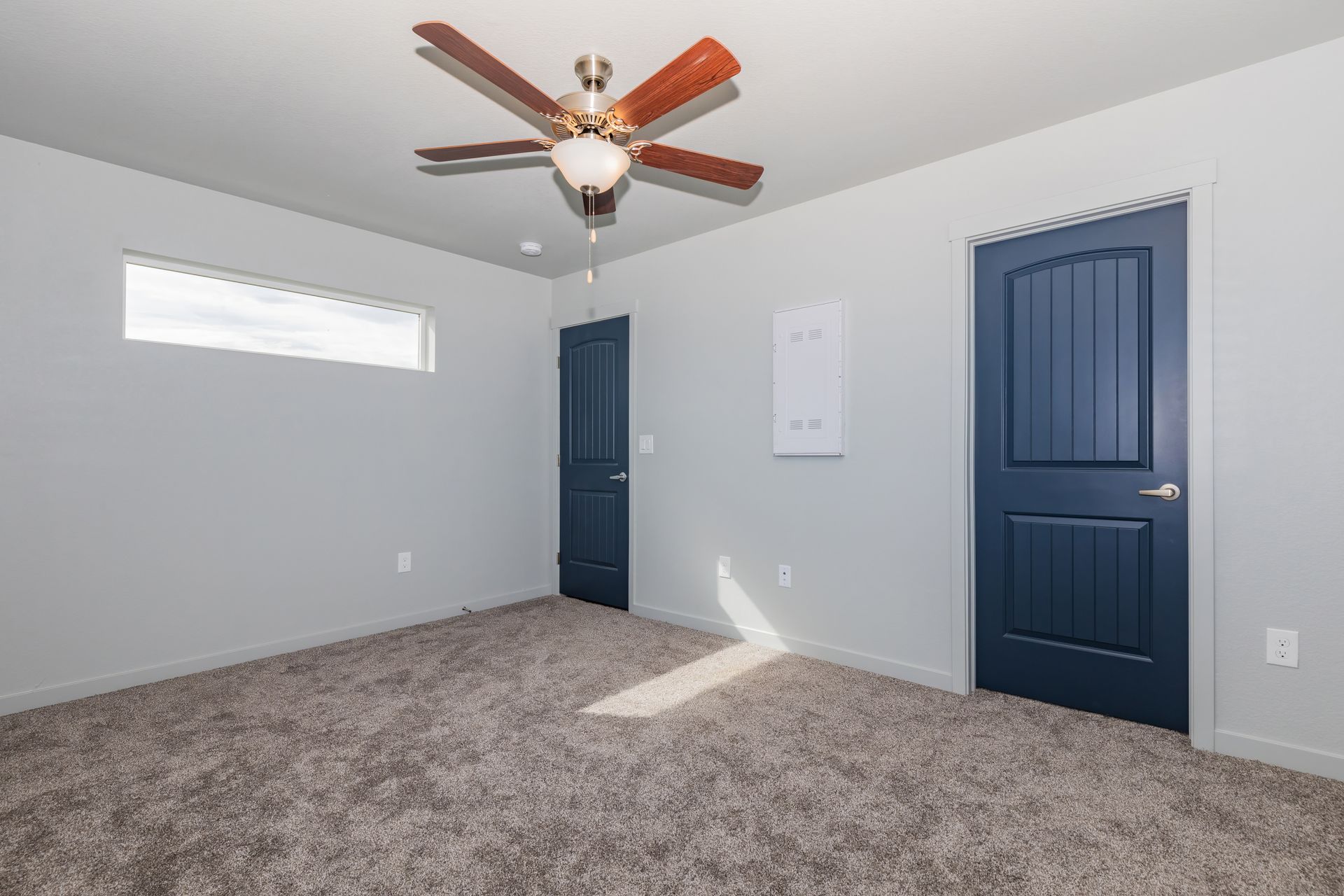 Empty carpeted bedroom with blue doors, gray walls, ceiling fan, and a small window.