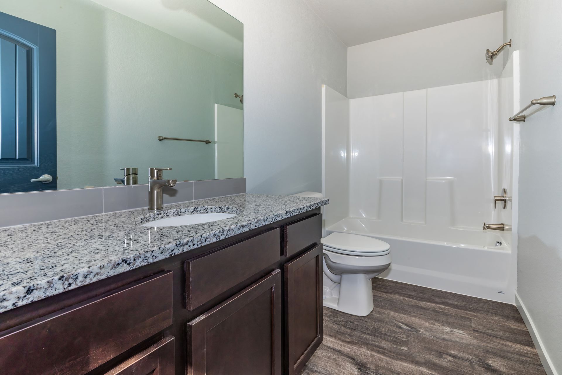 Modern bathroom with granite vanity, large mirror, toilet, and white shower curtain on wood-look flooring