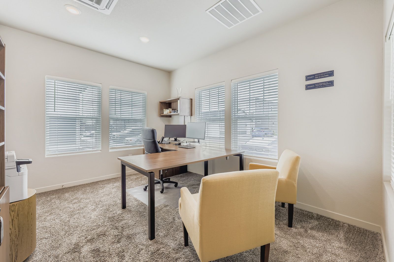 Bright home office with desk, computer, and two cream chairs by large windows.