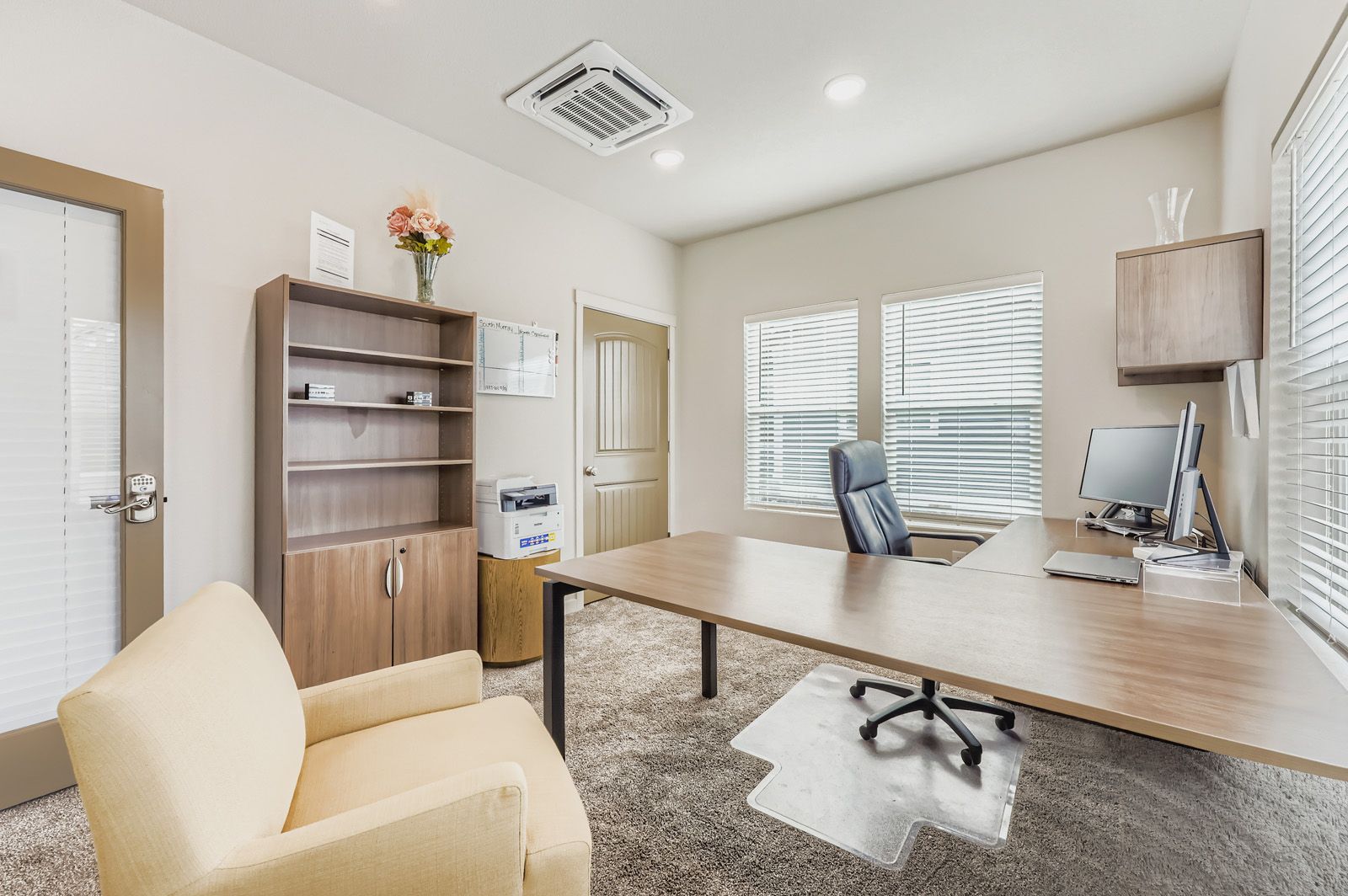 Modern home office with desk, chair, shelving, and light wood cabinetry near windows
