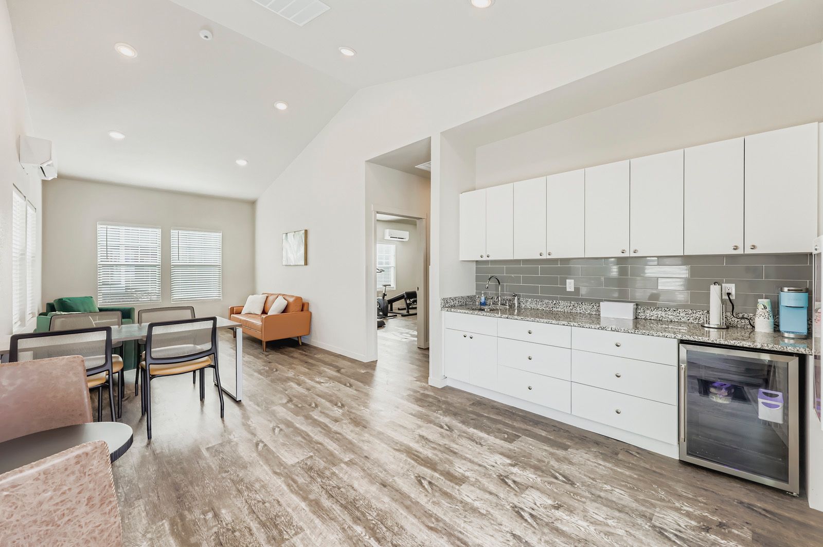Bright open kitchen and dining area with white cabinets, gray tile backsplash, and wood-look floors.