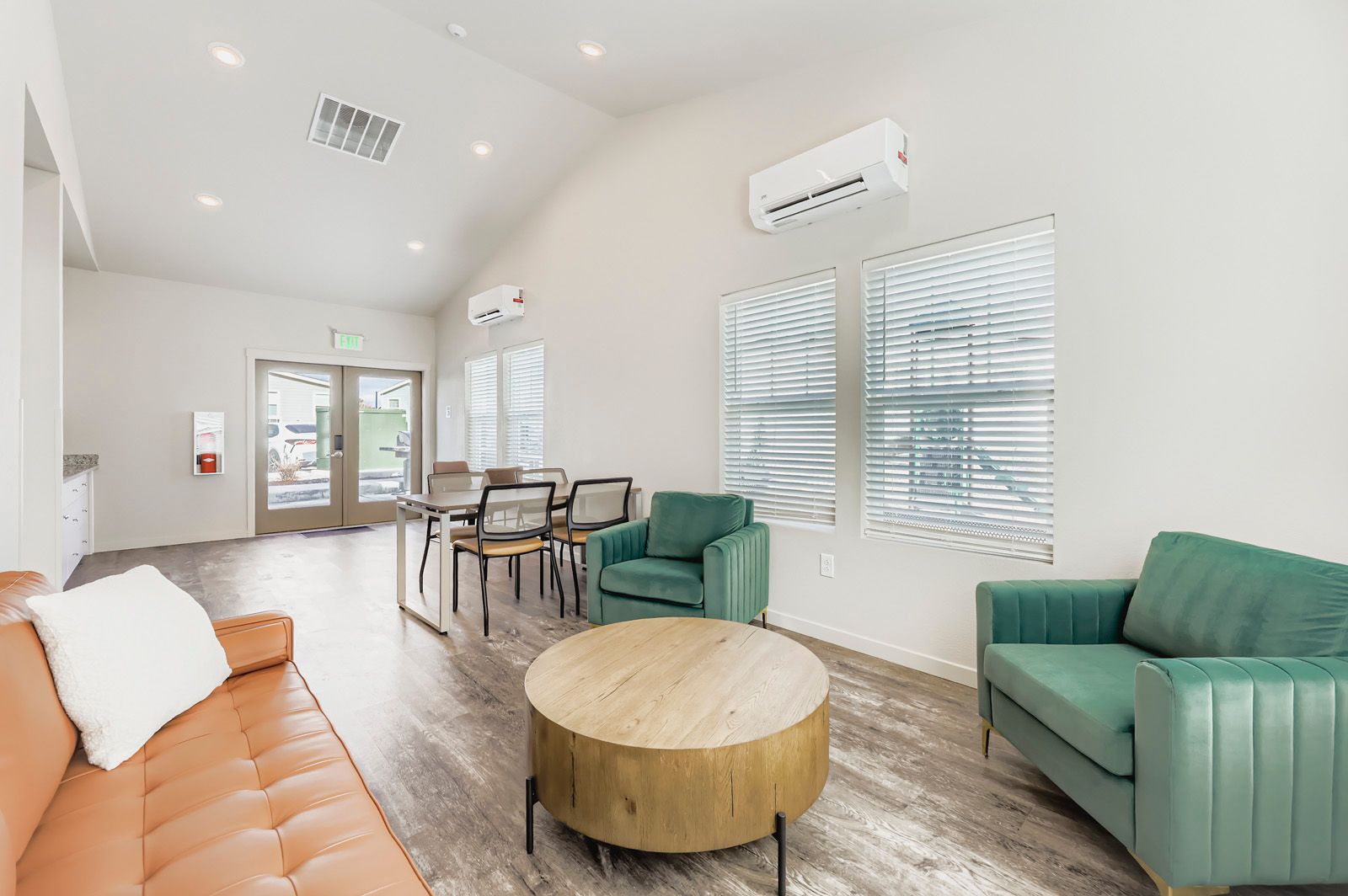 Bright waiting room with green and orange chairs, round coffee table, dining table, and large windows