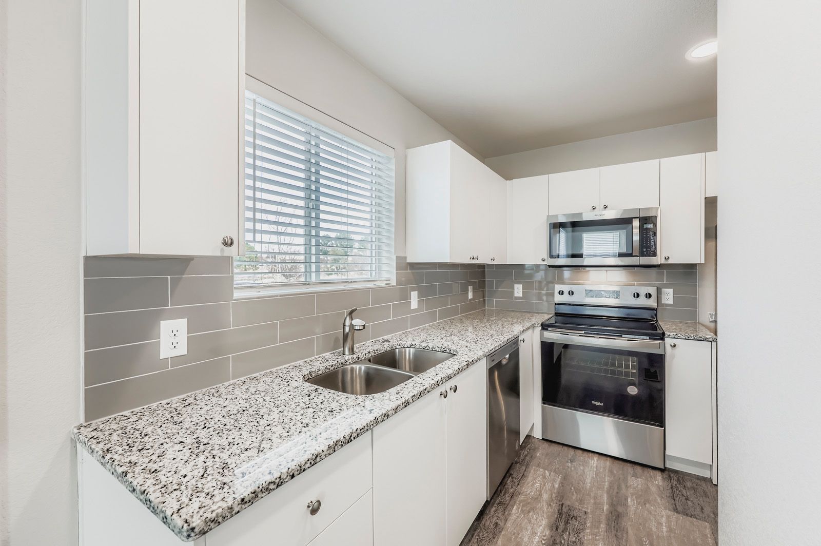 Bright modern kitchen with white cabinets, granite counters, gray backsplash, and stainless steel appliances.