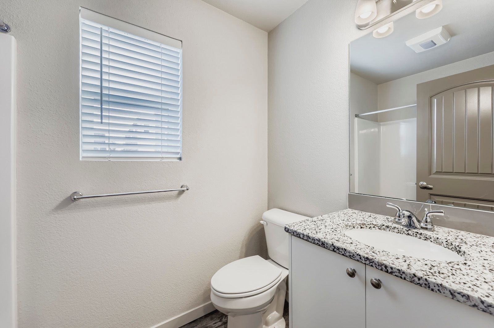 Bright bathroom with window, toilet, and granite vanity beside a large mirror.