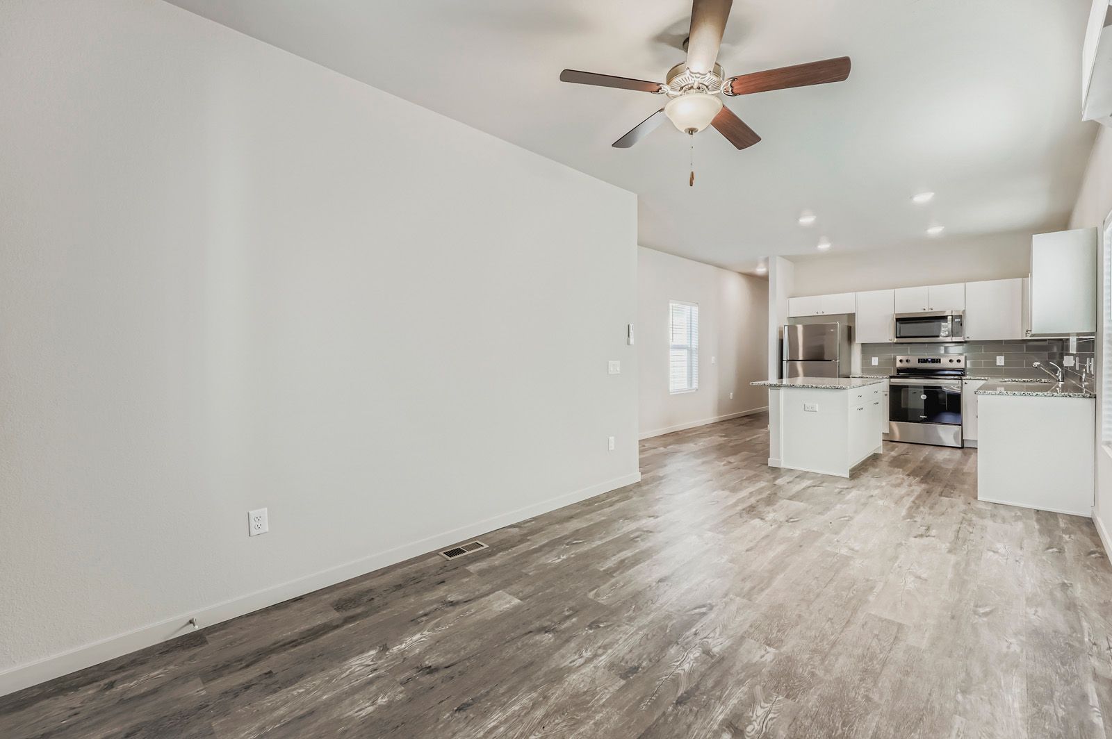 Empty modern kitchen and living area with wood-look flooring and ceiling fan