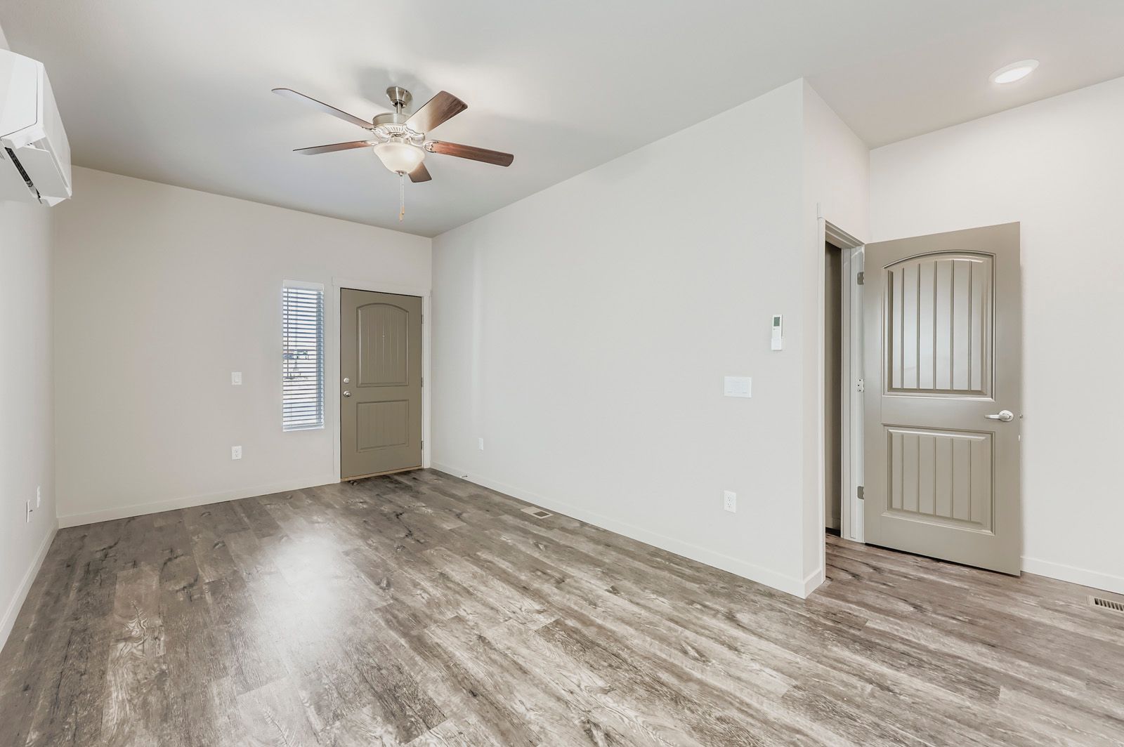 Empty bedroom with light gray walls, wood-look floors, ceiling fan, and closed doors