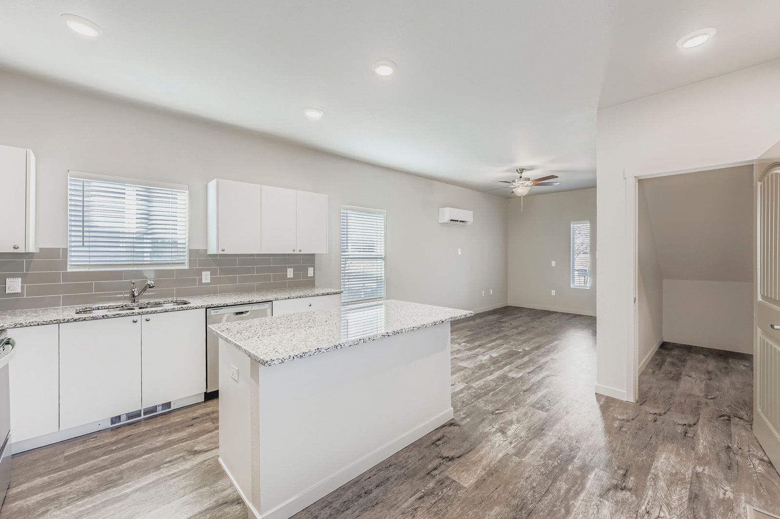 Bright, empty modern kitchen with white cabinets, gray tile floor, island, and recessed lighting