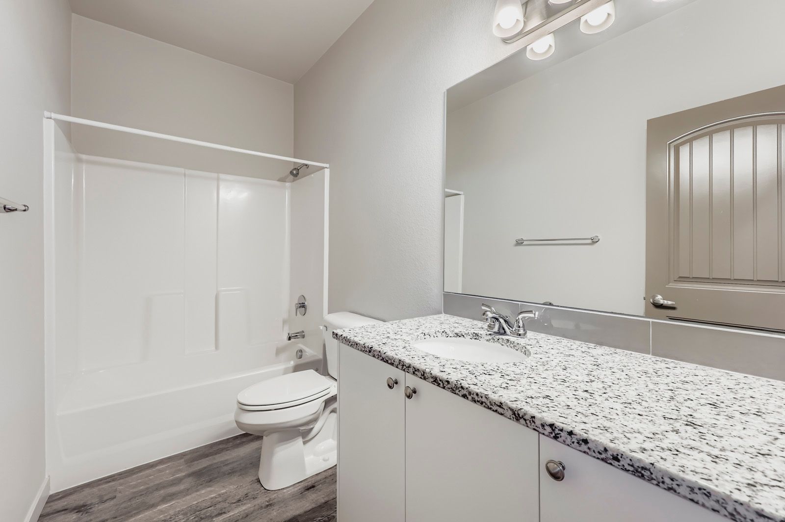 Bright bathroom with white vanity, speckled countertop, mirror, toilet, and bathtub shower combo.