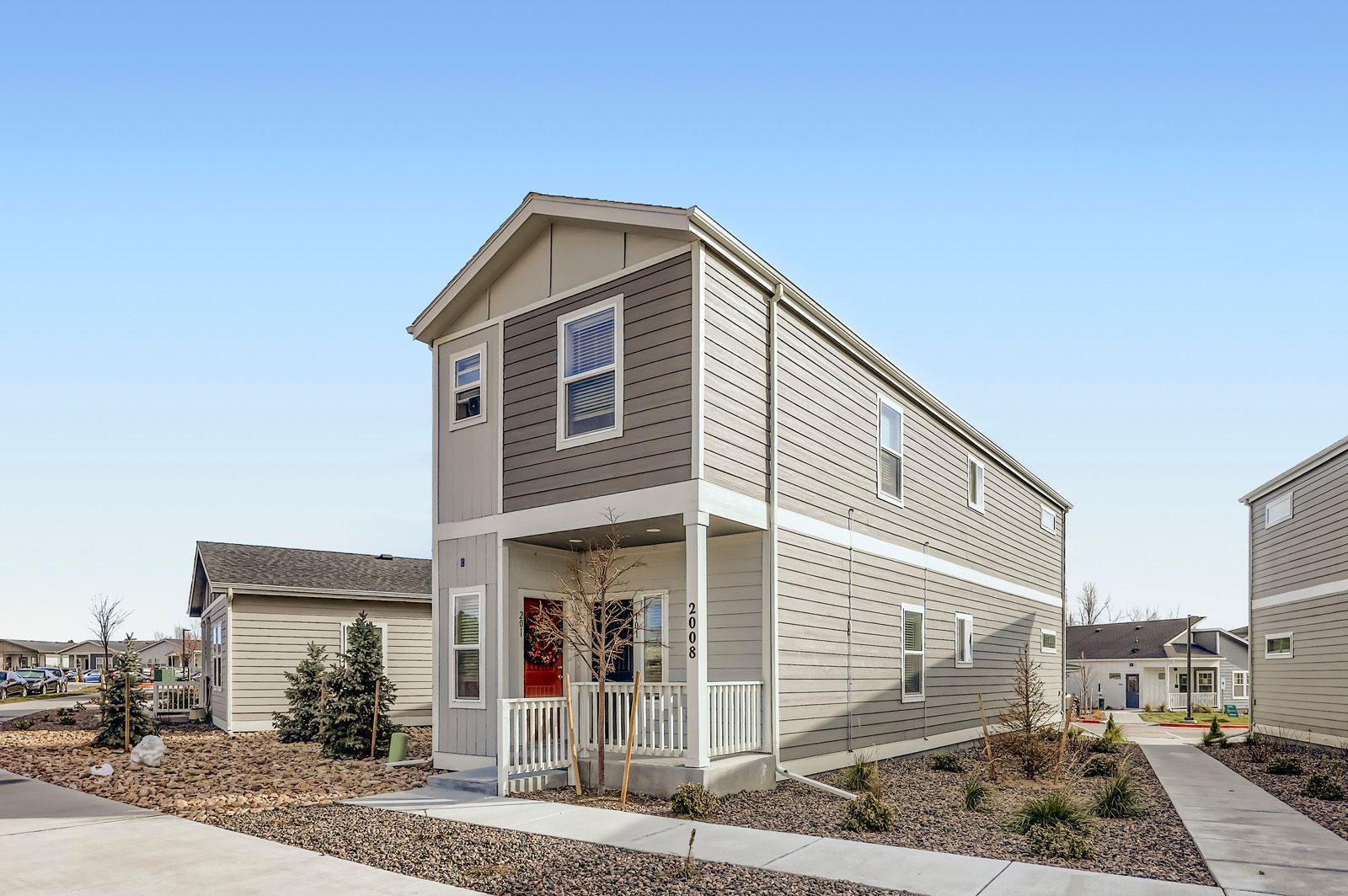 Modern two-story beige house exterior with porch, white trim, and landscaped front yard under a clear blue sky