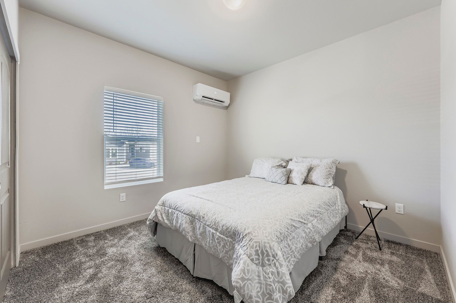 Bright bedroom with a bed, window, wall-mounted AC, and gray carpet