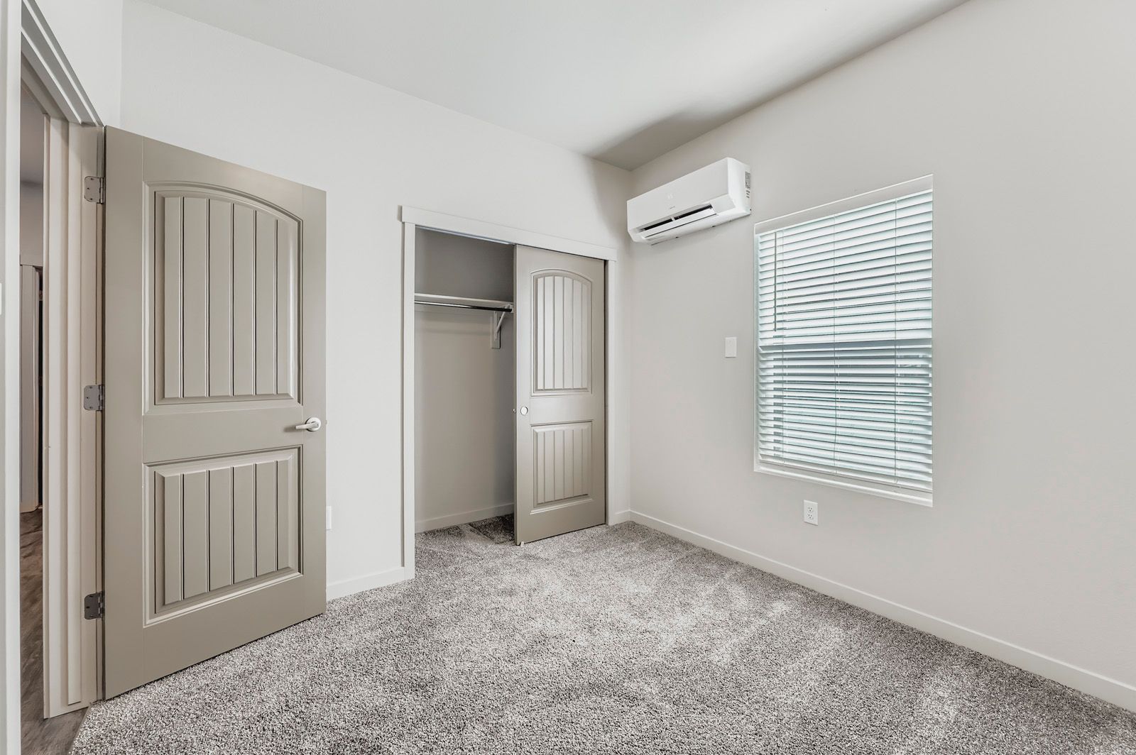Empty beige bedroom with open closet, carpet, and window blinds