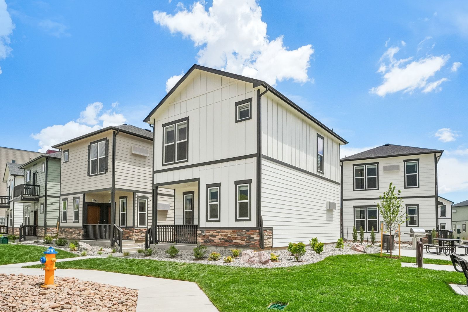 Row of modern two-story townhomes with white siding, stone accents, and landscaped lawns under a blue sky