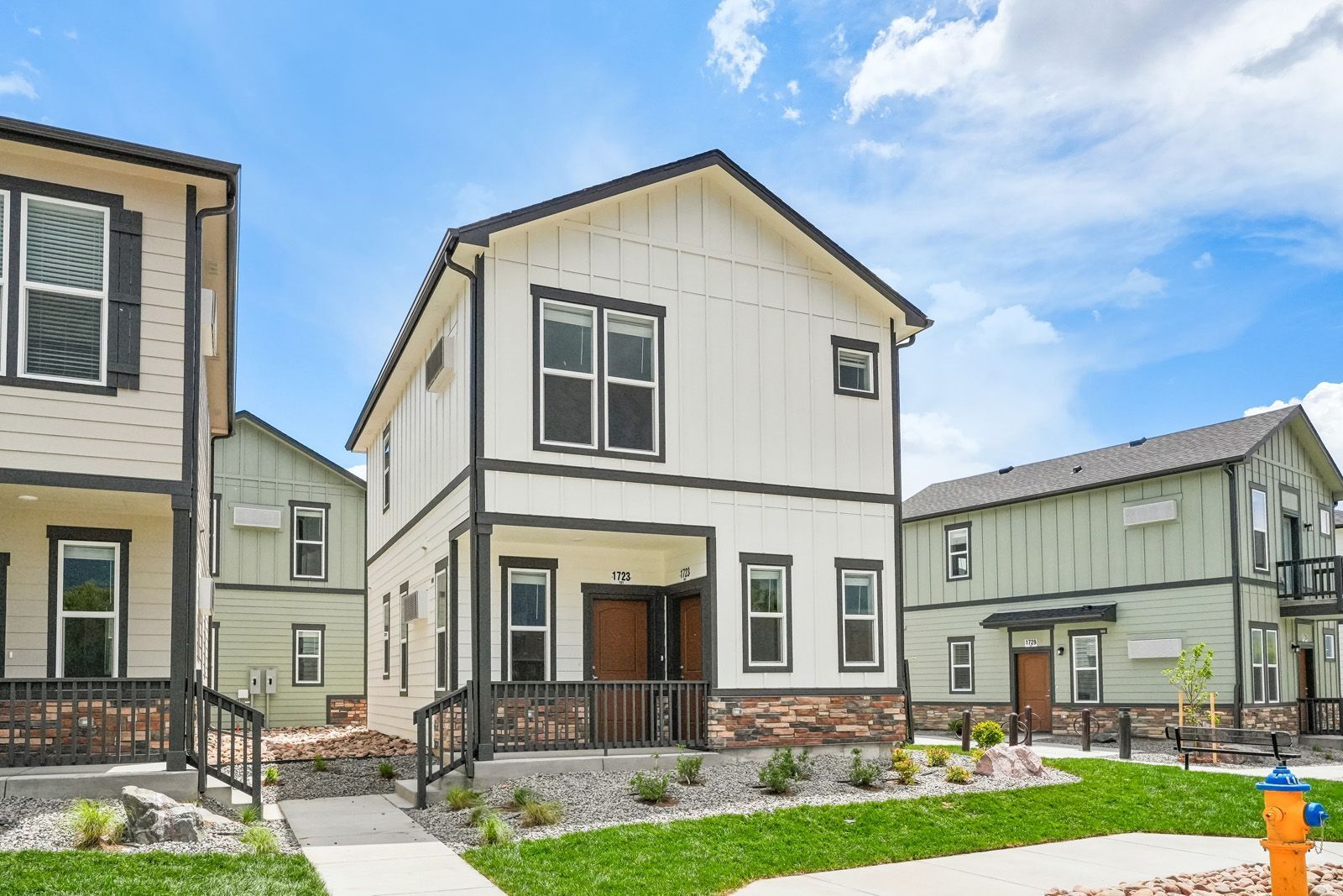 Row of modern two-story townhouses with front porches and green lawns under a blue sky