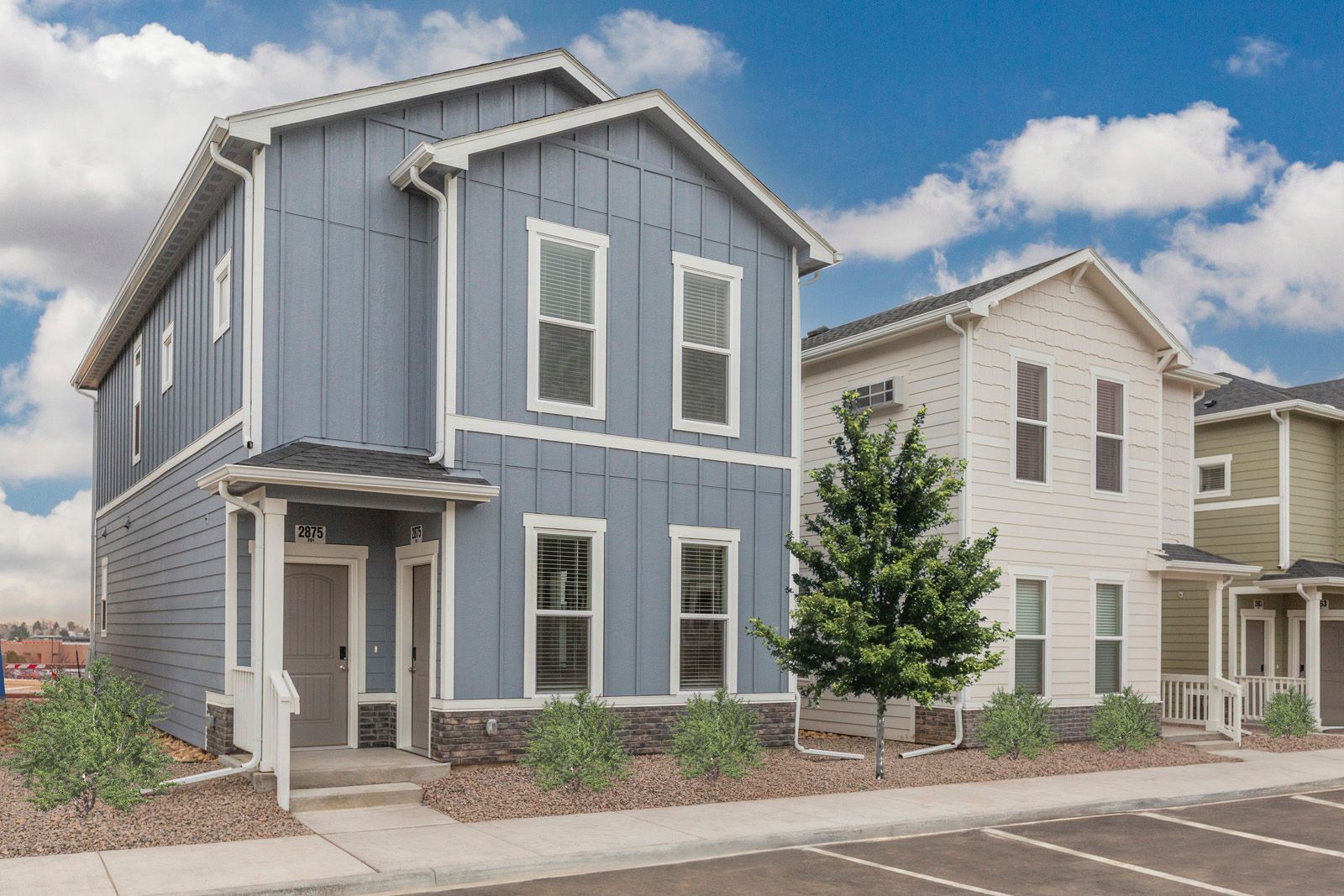 Two-story blue and white townhomes with a small tree and sidewalk in front