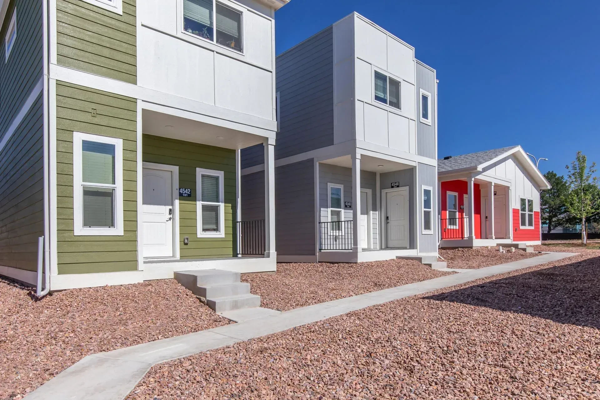 Row of modern townhouse homes with colorful facades and a gravel walkway under a clear blue sky