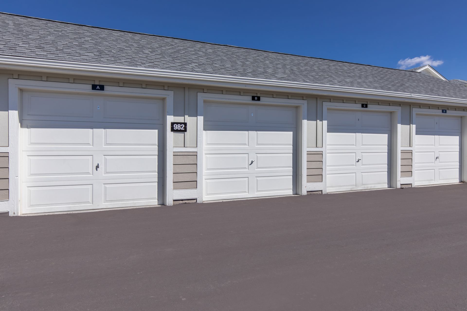 Row of white garage doors on a building with a gray shingled roof under a clear blue sky